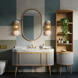 A curved bathroom vanity featuring Carrara marble top and a cane-front wooden cabinet with gold accents.