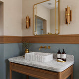 A fluted Carrara marble basin sits atop a rattan wood vanity, combining Italian luxury with artisanal craftsmanship.